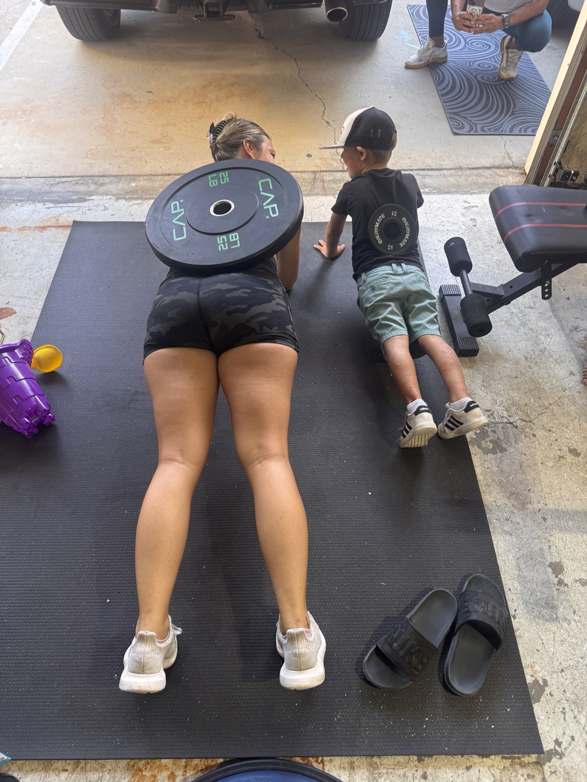 Woman training in a garage gym while a child joins her on the mat